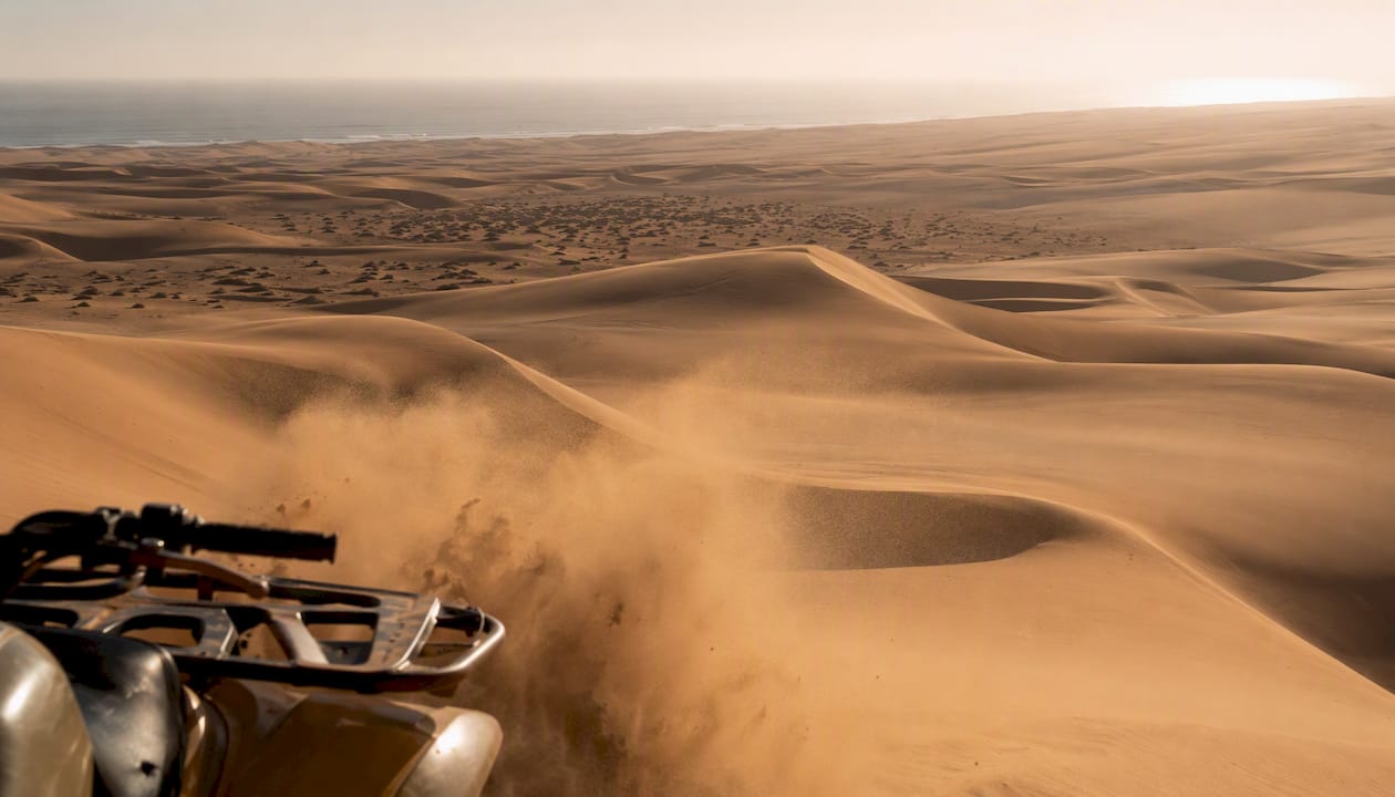 Partial quad bike silhouette kicking up sand on coastal dunes near Swakopmund