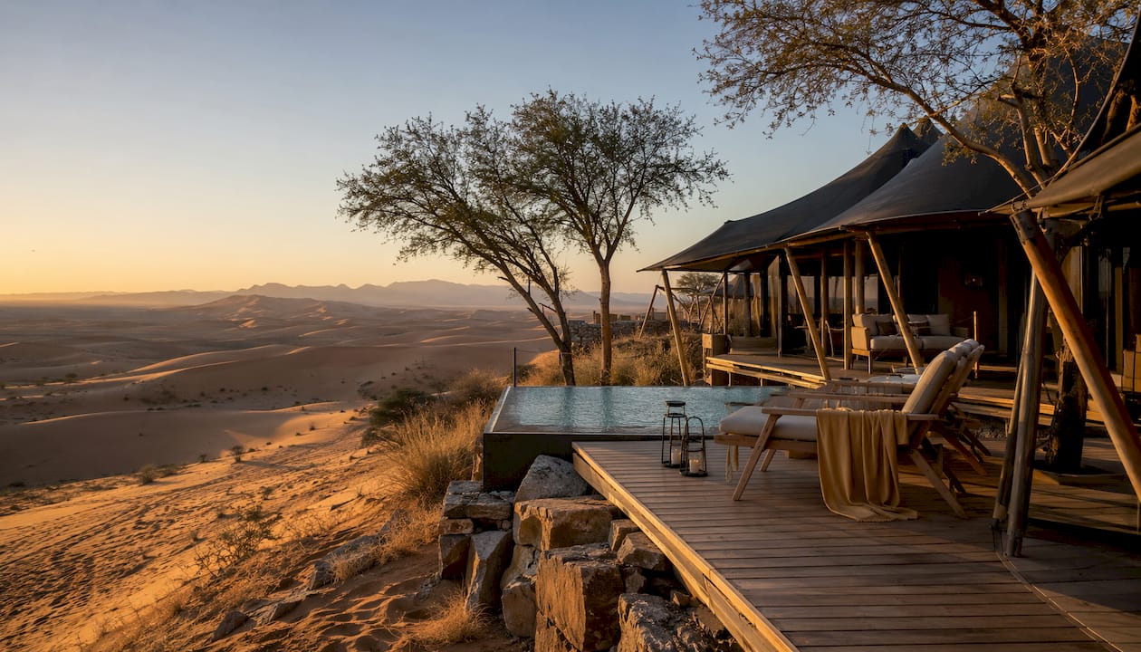 Luxury desert lodge with dunes and safari vehicle at sunset
