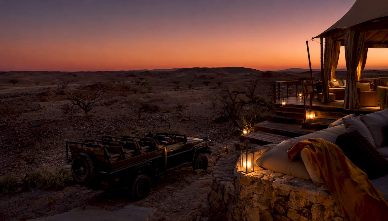 Safari vehicle by lodge with acacia plains at dusk.