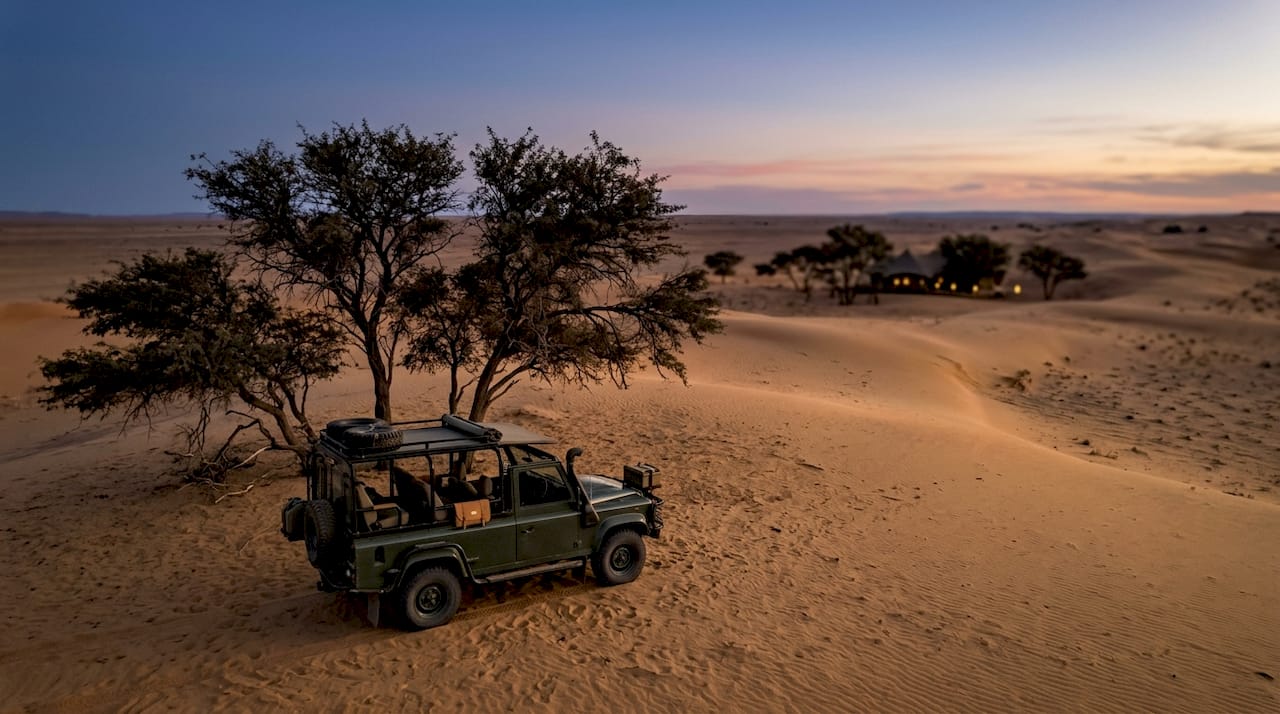 Safari vehicle by acacia trees at dusk