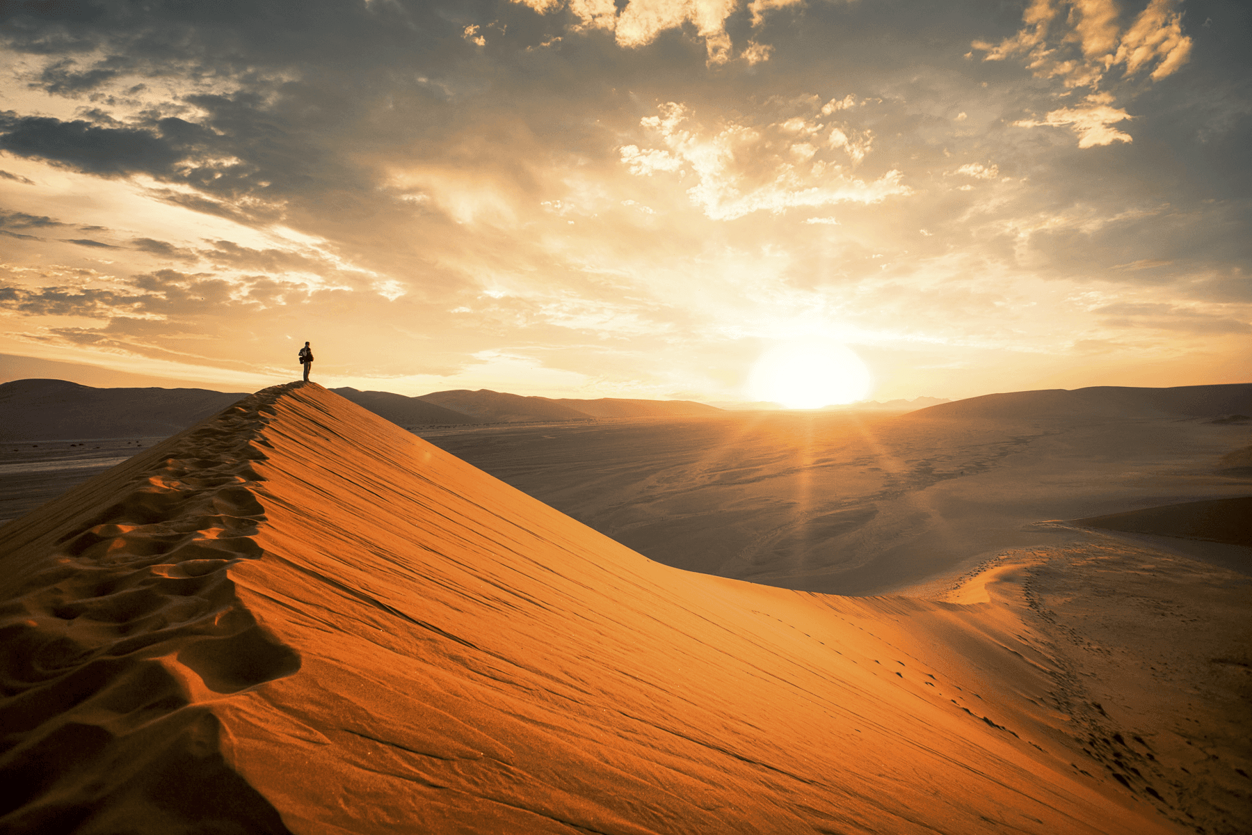 Man standing on sand dune in namibia watching the sun set