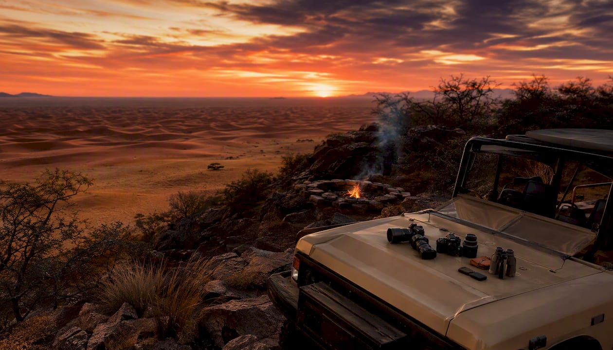 Safari vehicle parked by acacia trees at sunset