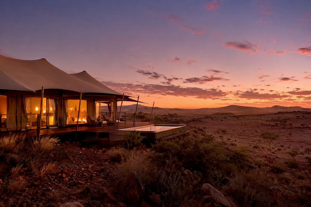 Canvas tent camp on wooden platform in red gravel desert